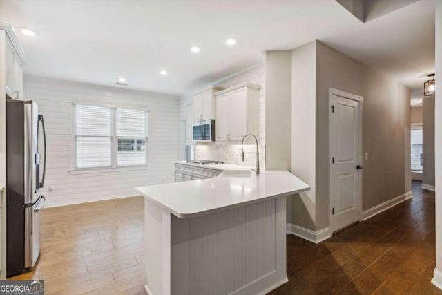 kitchen featuring white cabinetry, dark hardwood / wood-style floors, kitchen peninsula, decorative backsplash, and appliances with stainless steel finishes