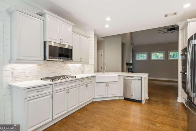 kitchen featuring kitchen peninsula, stainless steel appliances, ceiling fan, sink, and white cabinets