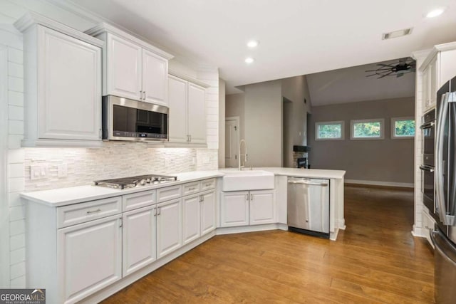 kitchen featuring kitchen peninsula, stainless steel appliances, light hardwood / wood-style floors, sink, and white cabinets