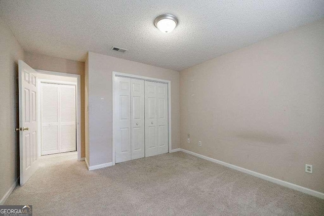 unfurnished bedroom with light colored carpet, a textured ceiling, and a closet