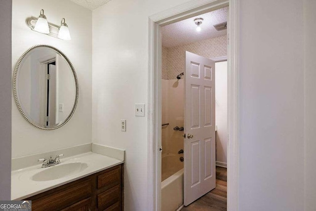 bathroom featuring hardwood / wood-style floors, a textured ceiling, shower / washtub combination, and vanity