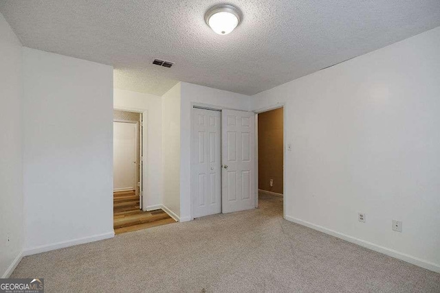 unfurnished bedroom with light carpet, a textured ceiling, and a closet