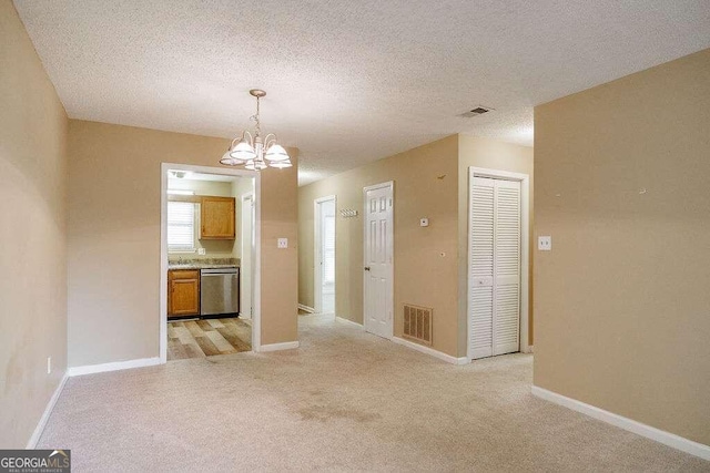 interior space featuring stainless steel dishwasher, hanging light fixtures, a textured ceiling, and light carpet