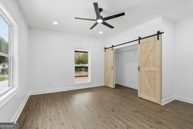 unfurnished bedroom featuring dark wood-type flooring, ceiling fan, a closet, and a barn door