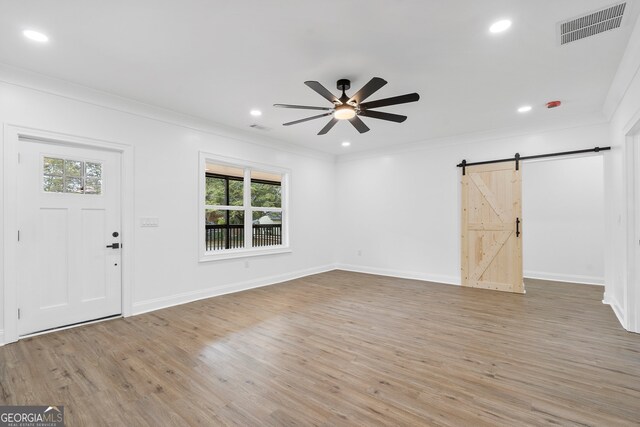 foyer entrance with light wood-type flooring, a barn door, ceiling fan, and plenty of natural light