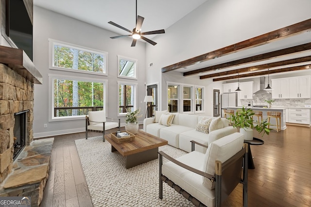 living room featuring ceiling fan, a towering ceiling, a stone fireplace, and light hardwood / wood-style flooring