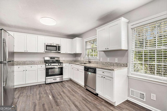 kitchen with stainless steel appliances, light stone counters, sink, dark hardwood / wood-style floors, and white cabinetry