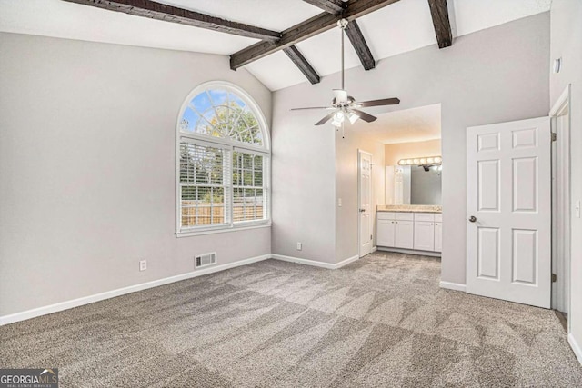 interior space featuring connected bathroom, light colored carpet, and vaulted ceiling with beams