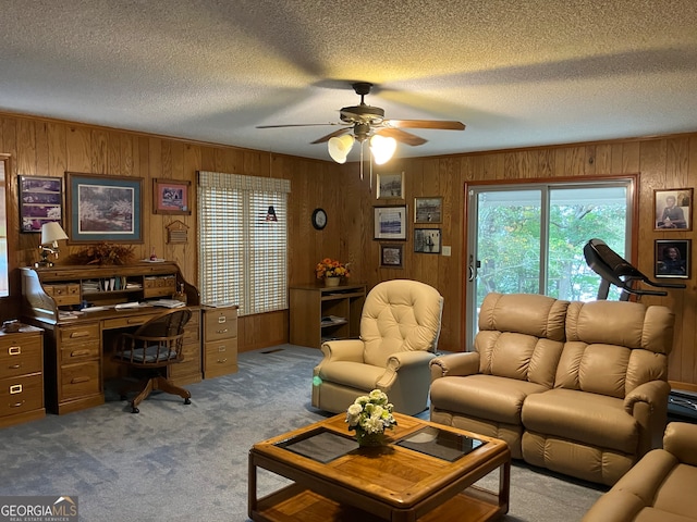 carpeted living room with a textured ceiling, wooden walls, and ceiling fan