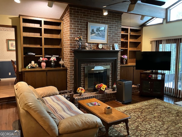 living room featuring vaulted ceiling with skylight, hardwood / wood-style flooring, ceiling fan, and a fireplace