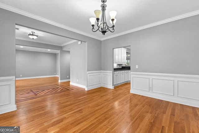 spare room featuring crown molding, light hardwood / wood-style floors, and an inviting chandelier