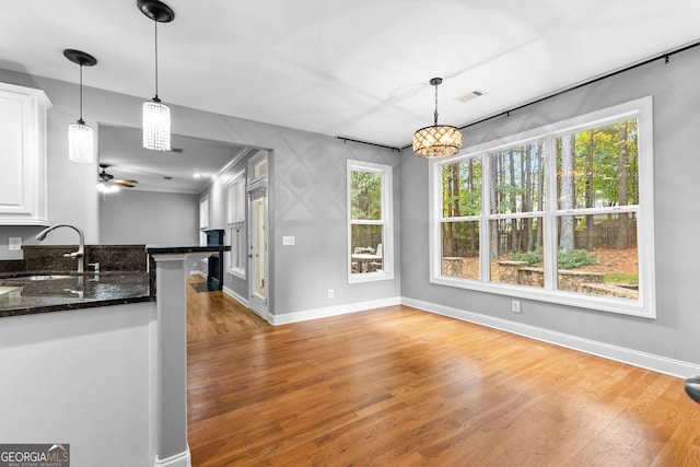 kitchen with light wood-type flooring, sink, dark stone countertops, white cabinets, and hanging light fixtures