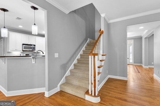 stairway featuring hardwood / wood-style flooring, ornamental molding, and sink