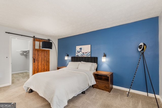 carpeted bedroom with a walk in closet, a closet, a textured ceiling, and a barn door