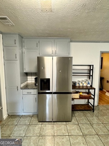 kitchen featuring dark stone countertops, stainless steel refrigerator with ice dispenser, a textured ceiling, and white cabinets