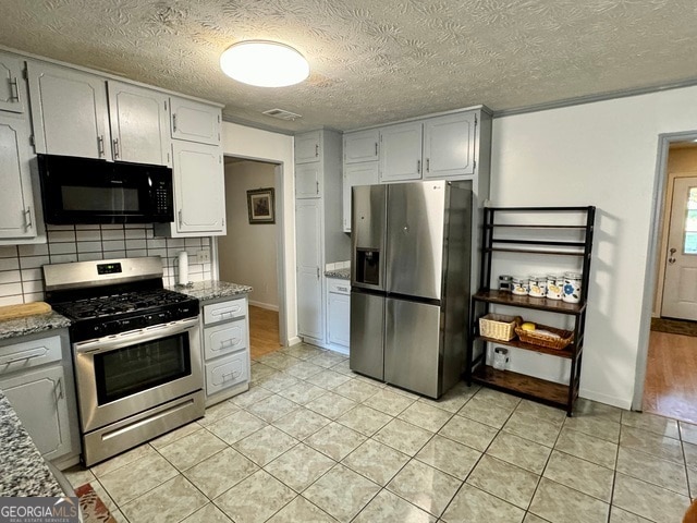kitchen featuring stainless steel appliances, a textured ceiling, tasteful backsplash, light tile patterned floors, and stone countertops