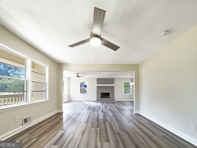 unfurnished living room featuring dark wood-type flooring, ceiling fan, and a brick fireplace