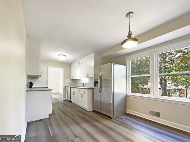 kitchen featuring hardwood / wood-style floors, white cabinets, hanging light fixtures, and stainless steel appliances