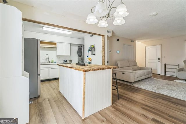 kitchen featuring stacked washer / dryer, wood counters, pendant lighting, white cabinets, and light hardwood / wood-style flooring