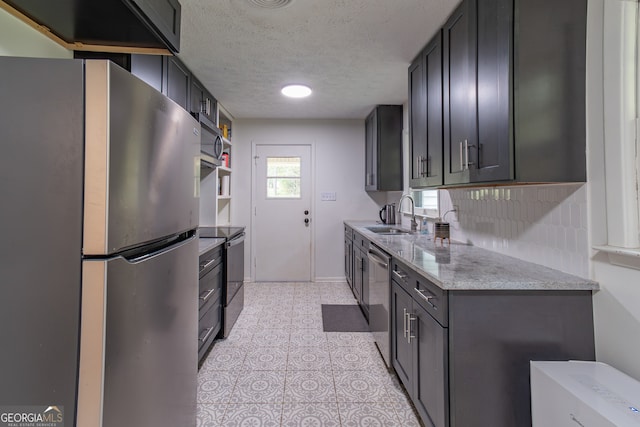 kitchen featuring appliances with stainless steel finishes, a textured ceiling, light tile patterned floors, decorative backsplash, and sink