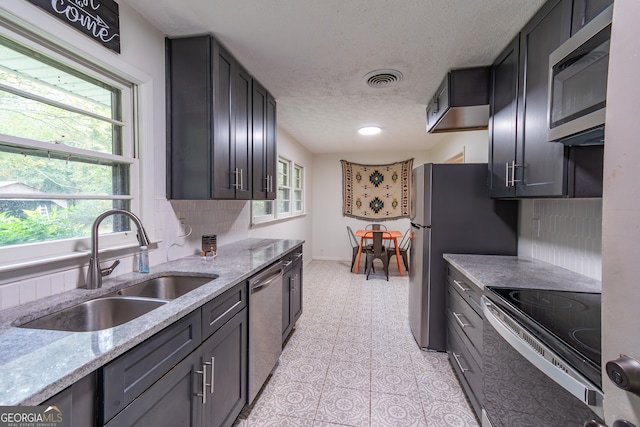 kitchen featuring light tile patterned flooring, sink, light stone counters, appliances with stainless steel finishes, and backsplash