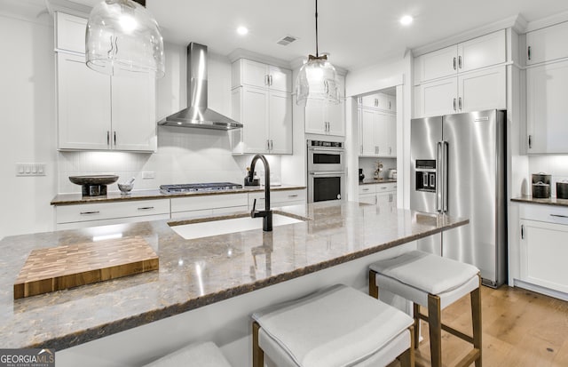 kitchen with stainless steel appliances, white cabinetry, dark stone counters, wall chimney exhaust hood, and light wood-type flooring