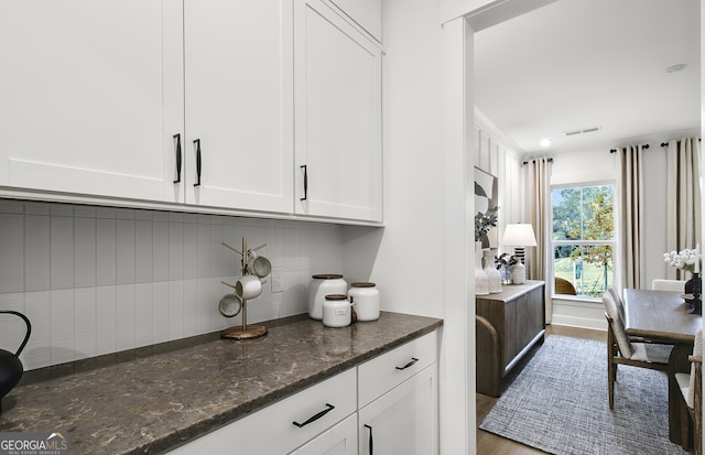 kitchen featuring dark stone countertops, decorative backsplash, wood-type flooring, and white cabinets