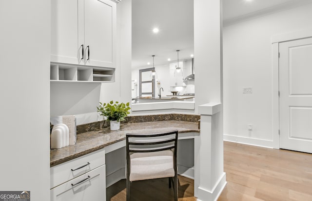 kitchen featuring pendant lighting, light hardwood / wood-style floors, white cabinets, and dark stone countertops