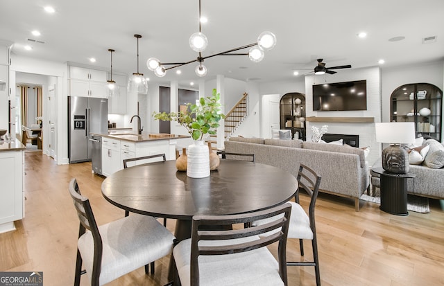 dining space featuring sink, light wood-type flooring, ceiling fan with notable chandelier, and a fireplace