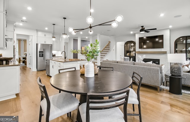 dining space featuring ceiling fan, sink, light hardwood / wood-style floors, and a fireplace