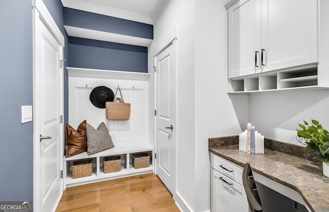 mudroom with built in desk, light wood-type flooring, and crown molding