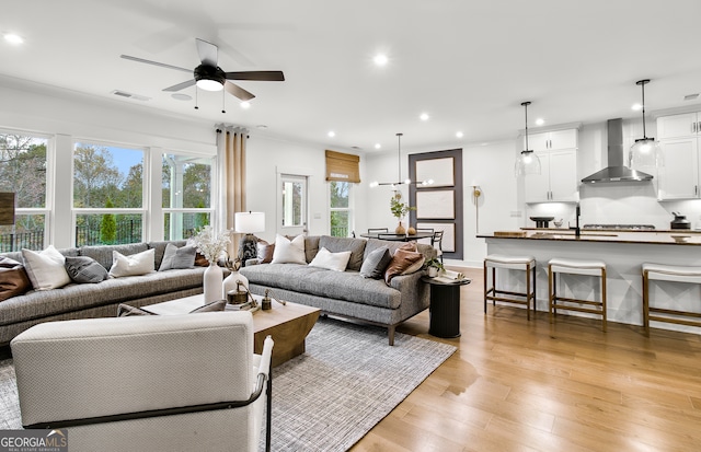 living room with ornamental molding, light wood-type flooring, a healthy amount of sunlight, and ceiling fan with notable chandelier