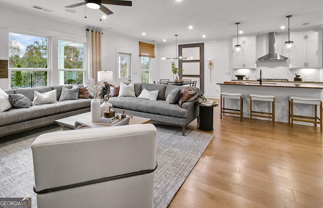 living room with ornamental molding, ceiling fan with notable chandelier, light hardwood / wood-style flooring, and sink