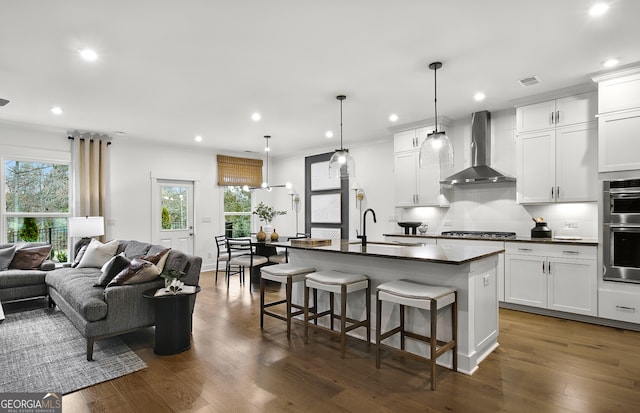 kitchen featuring decorative light fixtures, dark hardwood / wood-style flooring, sink, an island with sink, and wall chimney exhaust hood