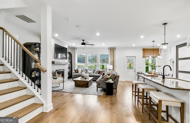 living room with light wood-type flooring, ceiling fan with notable chandelier, sink, and a fireplace