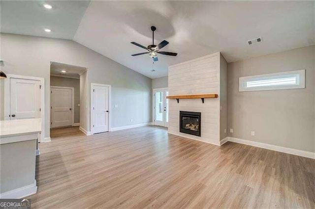 unfurnished living room with ceiling fan, a fireplace, lofted ceiling, and light wood-type flooring