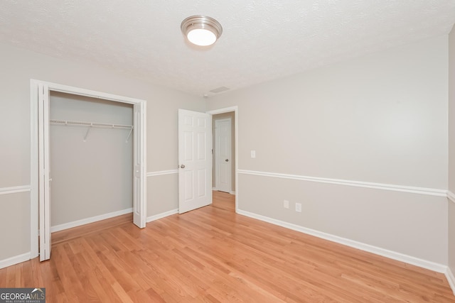 unfurnished bedroom featuring a closet, a textured ceiling, and light hardwood / wood-style flooring