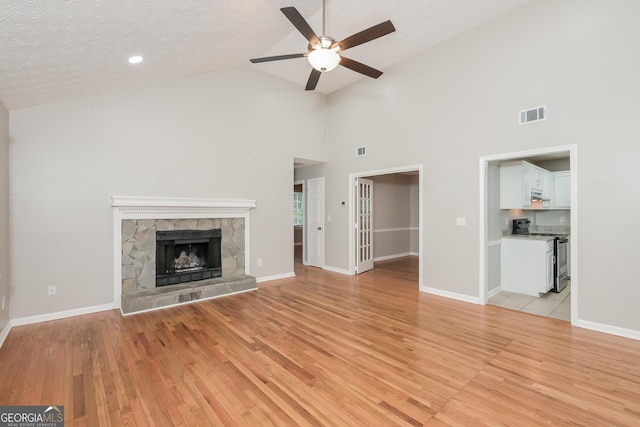 unfurnished living room featuring ceiling fan, high vaulted ceiling, light hardwood / wood-style floors, a textured ceiling, and a fireplace