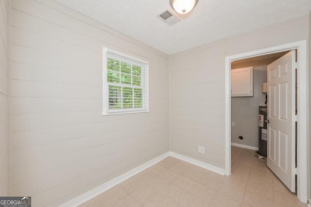 spare room with water heater, wood walls, and a textured ceiling