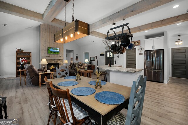 dining space featuring lofted ceiling with beams, sink, a fireplace, and light hardwood / wood-style flooring