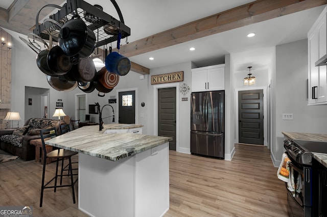 kitchen featuring light stone countertops, stainless steel fridge, black range with electric cooktop, sink, and white cabinets