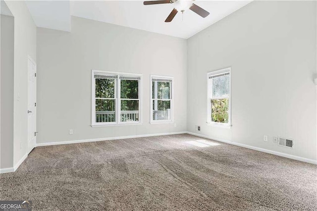 carpeted spare room with a wealth of natural light, a towering ceiling, and ceiling fan