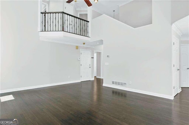 unfurnished living room with ceiling fan, a towering ceiling, dark wood-type flooring, and ornamental molding