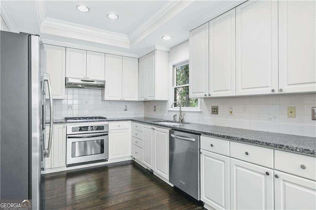 kitchen with appliances with stainless steel finishes, dark stone counters, sink, dark hardwood / wood-style floors, and white cabinetry