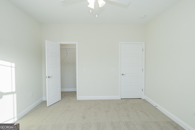 unfurnished bedroom with a spacious closet, light carpet, and ceiling fan