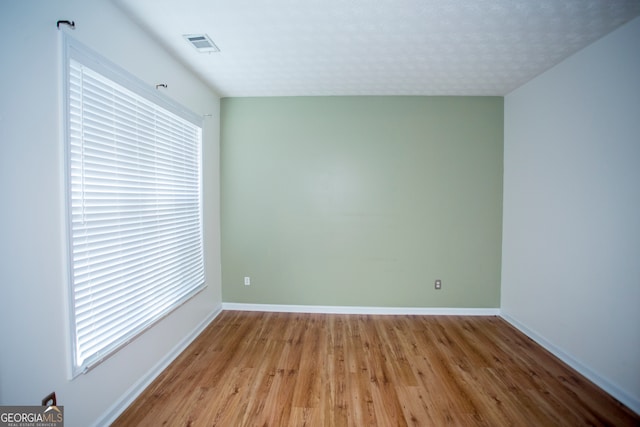 empty room with light wood-type flooring and a textured ceiling