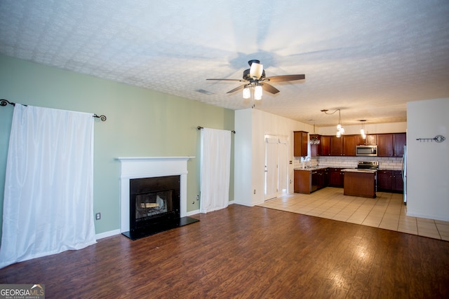 unfurnished living room with a textured ceiling, light wood-type flooring, ceiling fan, and sink