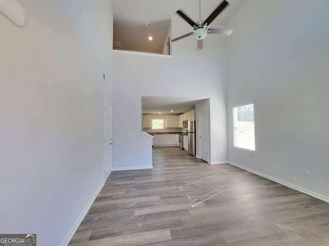 unfurnished living room with ceiling fan, light hardwood / wood-style flooring, and a towering ceiling