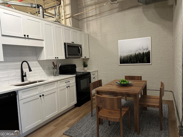 kitchen with brick wall, sink, black appliances, light hardwood / wood-style flooring, and white cabinets