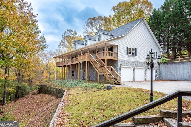 back of property with a garage, stone siding, driveway, stairway, and a lawn